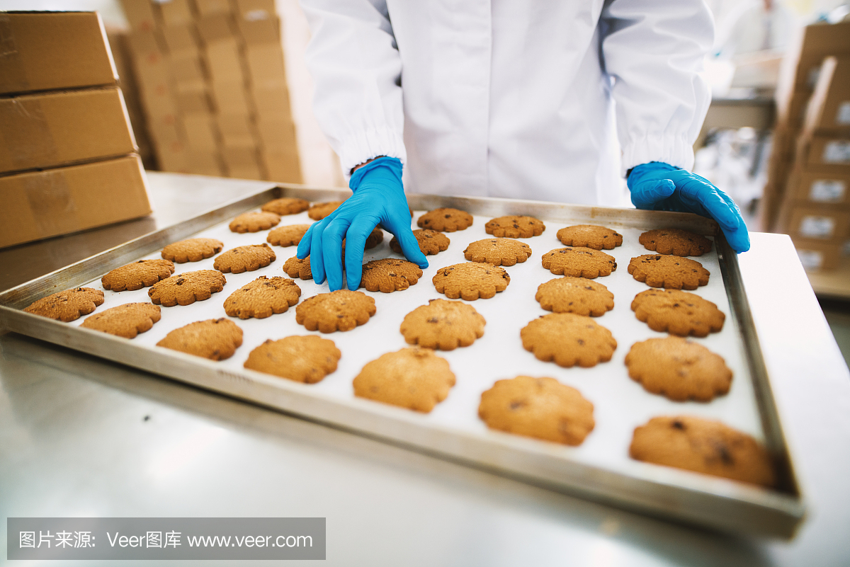 一个戴着蓝手套的工人正在把刚烤好的饼干从锅里拿下来,准备打包。